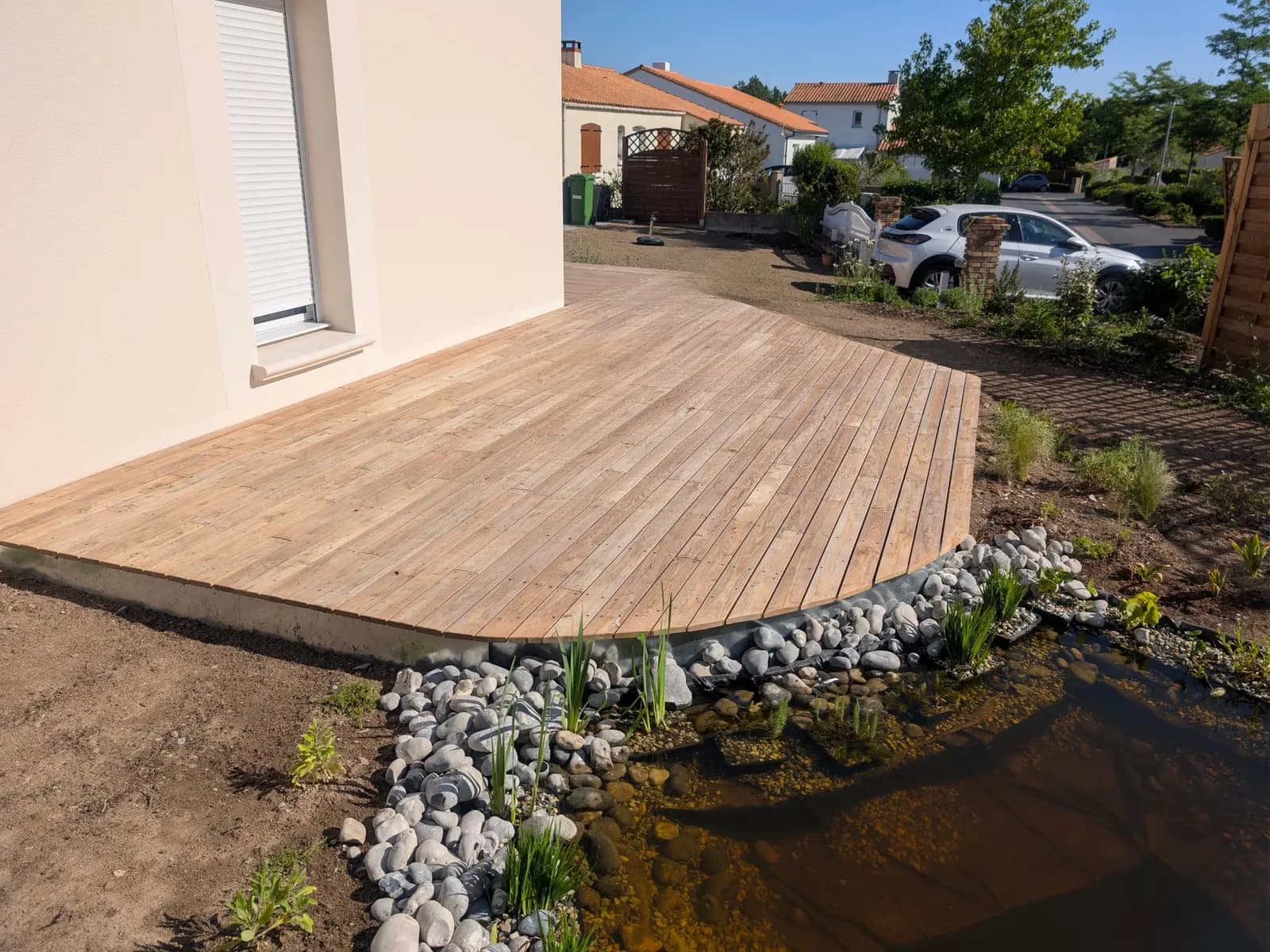 Terrasse en bois bordée d’une mare naturelle et de galets