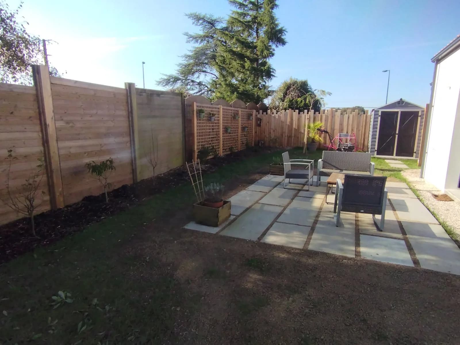 Terrasse en dalles et clôture en bois dans un jardin aménagé par Permapaysage